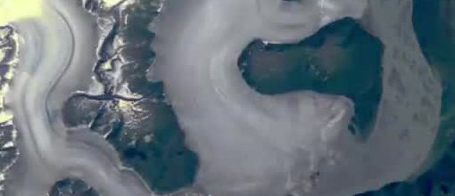 Satellite view of a glacier tongue bending between dark mountain ridges.