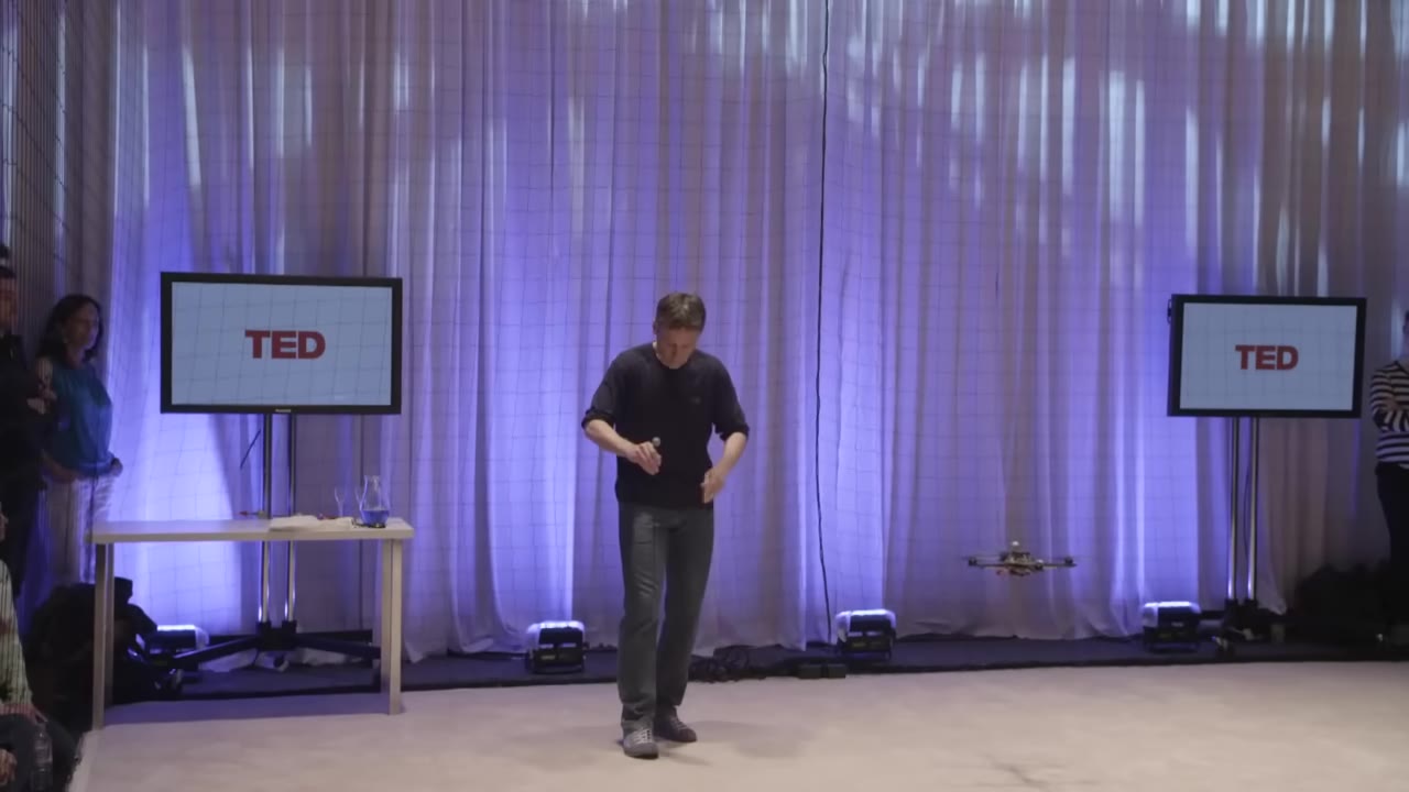 Quadcopter hovering beside a speaker inside a netted TED stage arena
