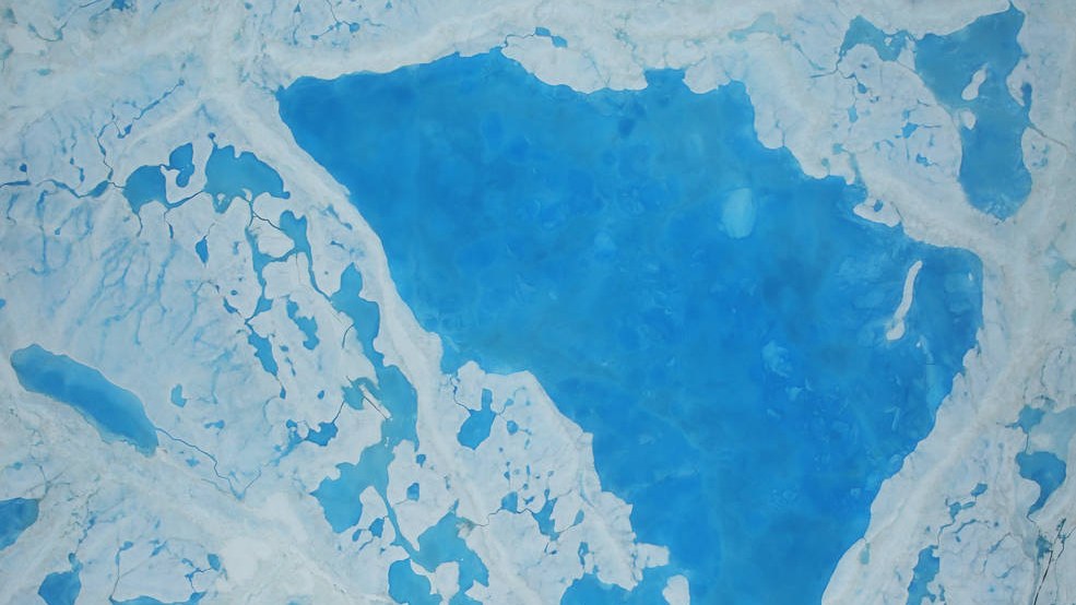 Aerial view of a large turquoise melt pond on broken Arctic sea ice.