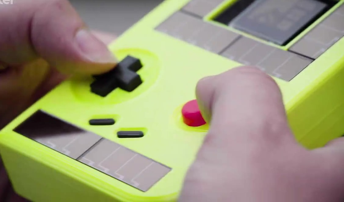 Hands holding a neon-yellow Game Boy prototype with solar panels around the screen