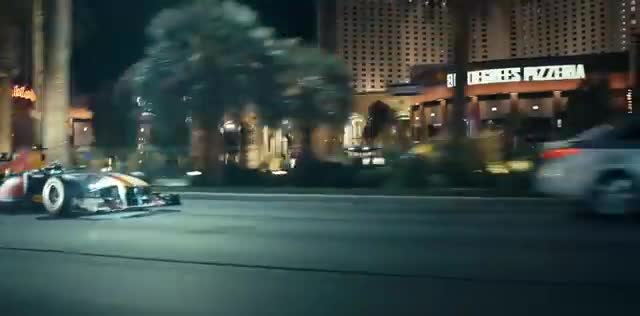 A Formula-style car driving a city street at night.