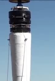 A white cylindrical mast with a dark stacked top against a blue sky.