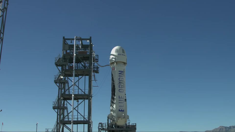 White New Shepard booster standing beside a launch tower during an abort test