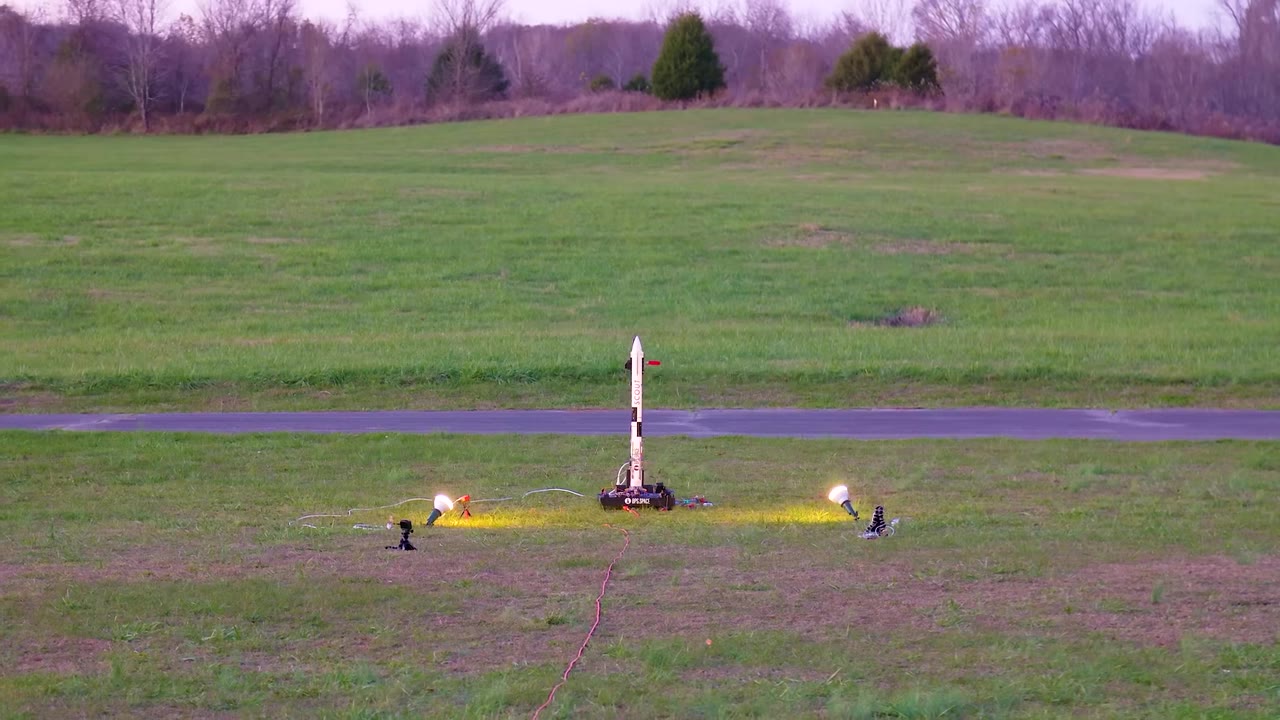 BPS.space Scout E model rocket standing on a pad in a grassy field at dusk