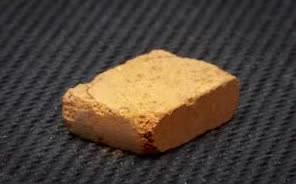 A small tan brick of compacted soil on a dark textured mat.