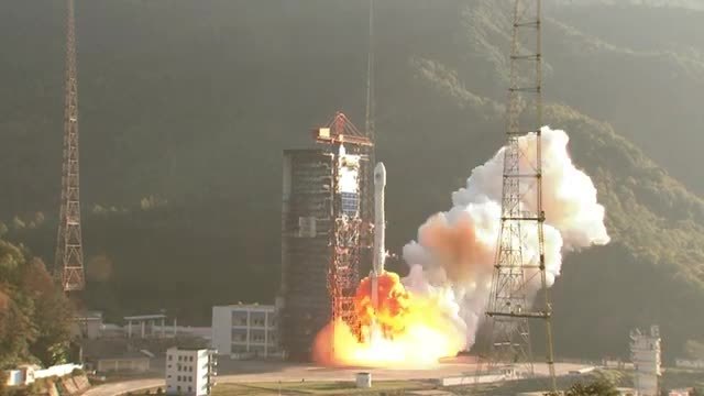 A Long March rocket lifting off beside its tower, with an orange flame and a white exhaust cloud.