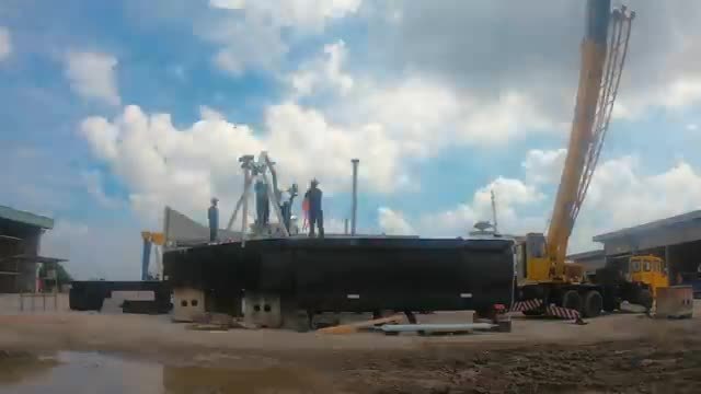 A black barge-like trash collector on stands, with a crane beside it.