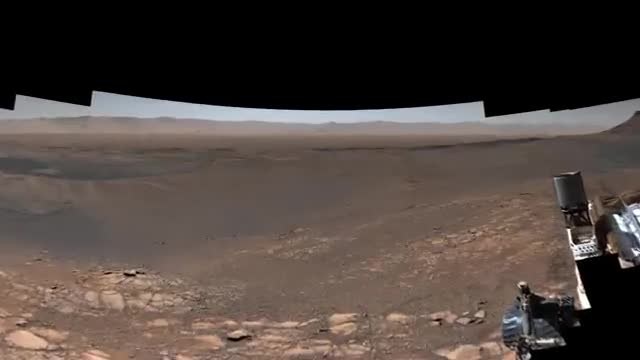 Wide Mars panorama of rocky ground and distant hills with part of the rover at the right edge