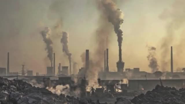 Factory stacks pouring smoke into a hazy sky.