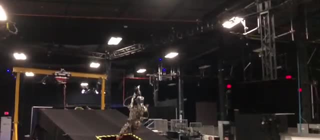 A humanoid robot flipping above a trampoline in a dark studio.