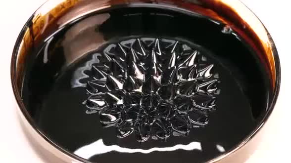 Black ferrofluid standing in spikes over a magnet