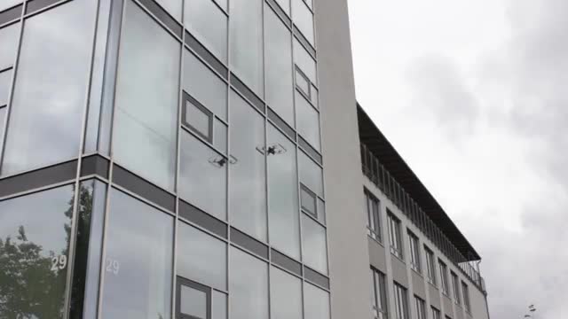 A small drone hovering against the glass face of an office building
