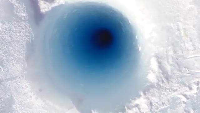 Round blue opening of a borehole in white ice