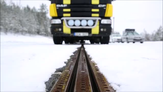 A metal rail in a snowy road ahead of a truck.
