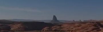 A dry red-rock canyon and a lone butte under a clear sky.