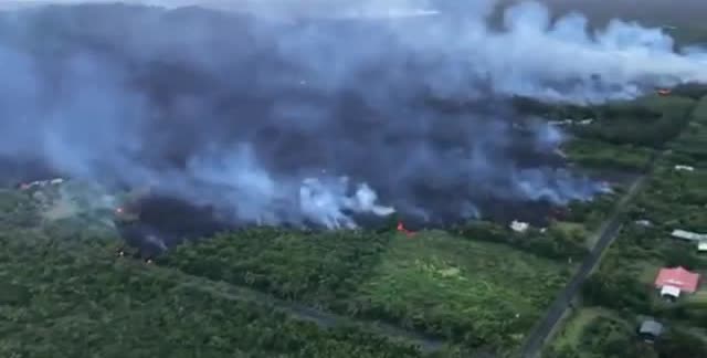Smoke over a lava flow moving through green land.