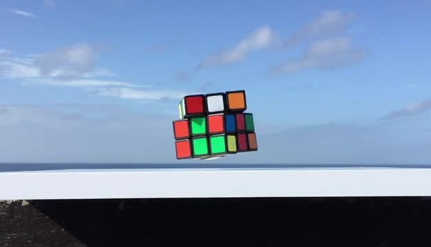 A scrambled Rubik cube hovering above a white rail with ocean and sky behind it