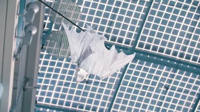 A white robotic bat hanging from a tether in a lab