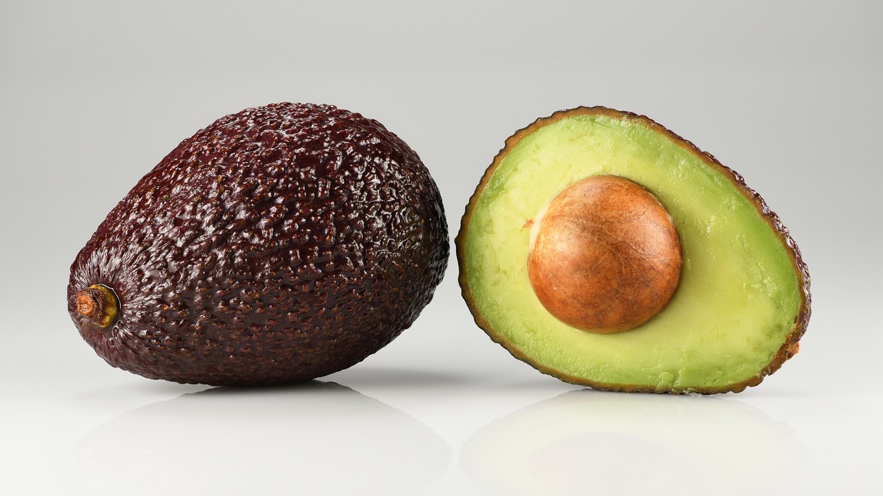 A whole Hass avocado next to a halved one