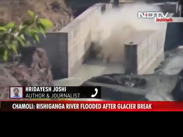 Muddy floodwater slamming into a concrete dam in a mountain valley