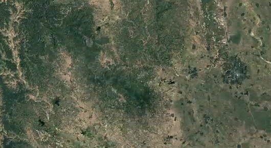Satellite view of fields, forest, and a growing city grid.