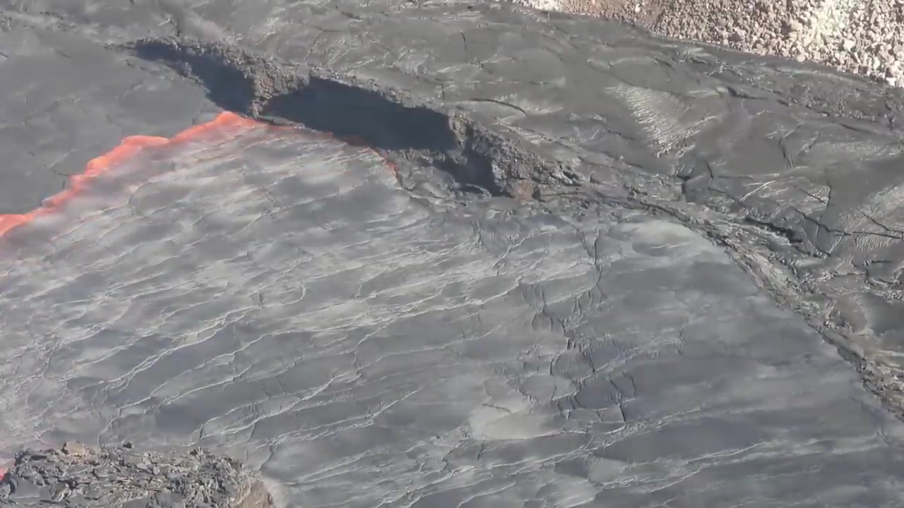 Orange molten lava streaming under a cracked dark crust on a lava lake