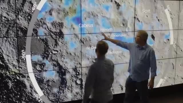Two people pointing at a lunar south-pole map labeled with craters including Cabeus and Shoemaker