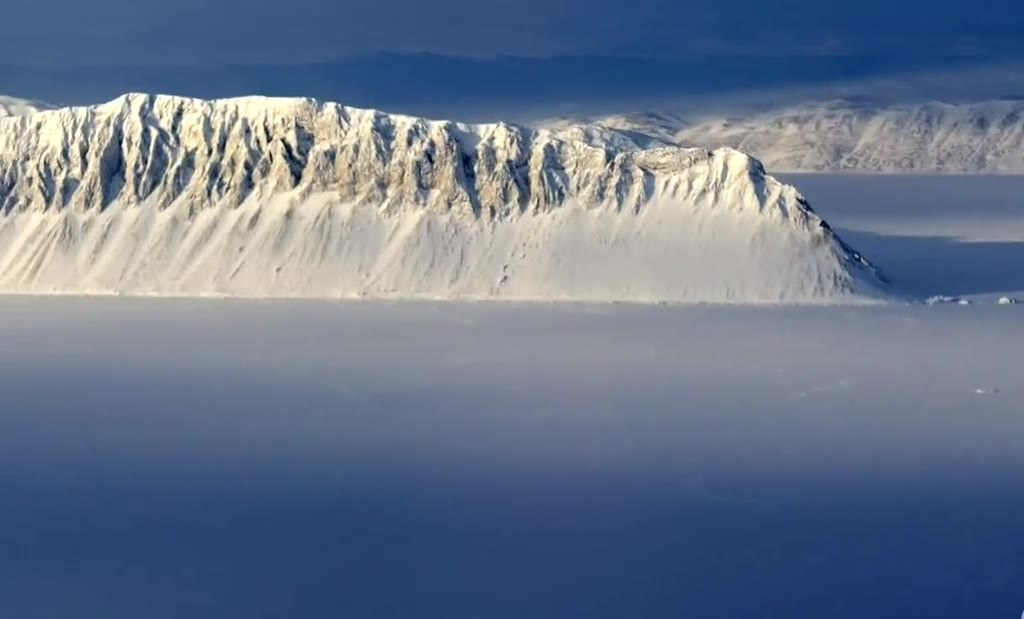 Snow-covered ice cliff rising out of a foggy Arctic sea