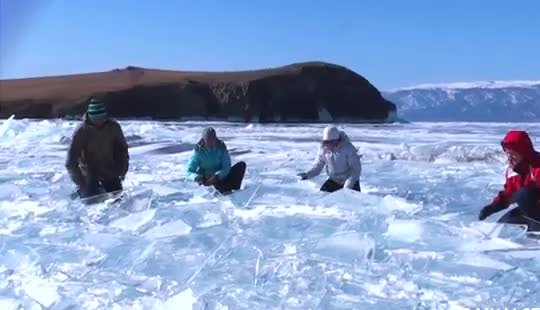 People on broken plates of clear lake ice under a blue sky.
