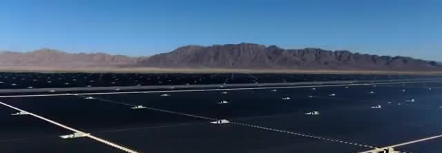 Rows of solar panels at a desert photovoltaic farm with mountains behind