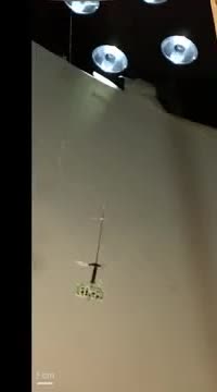 A tiny winged robot hanging from a wire under lab lights