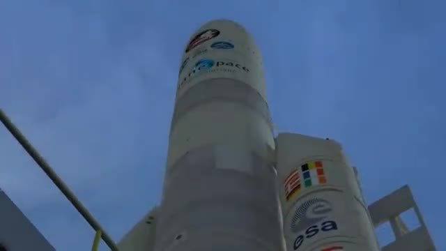 Looking up a white rocket and its side booster against a blue sky.