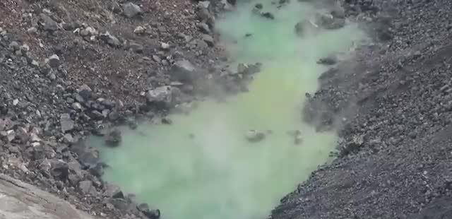 A green pool of water in a rocky volcanic crater.