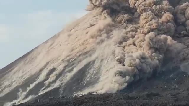 A pale ash cloud pouring down the flank of a volcano.