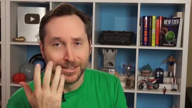 A presenter explaining batteries in front of a shelf of books and models.