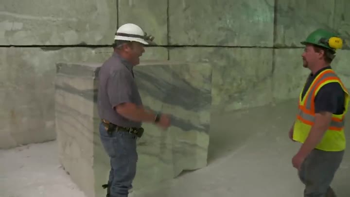 Two workers beside a large cut block of marble underground