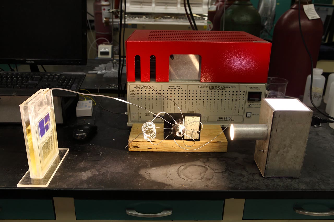 A lab bench with a clear cell, coiled tubing, and a lamp aimed at a metal chamber.