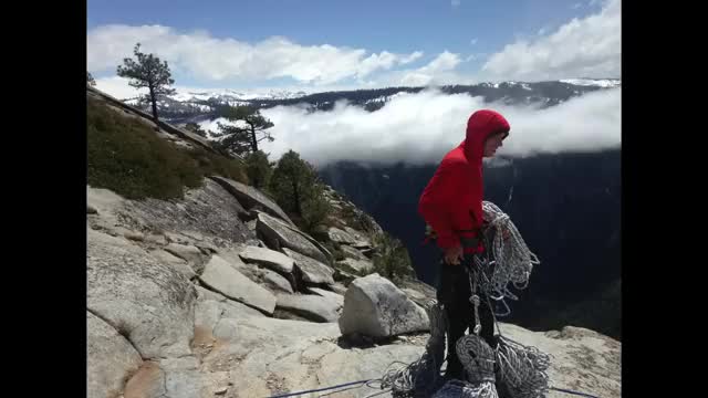 A climber with a coil of rope on a high granite ridge.