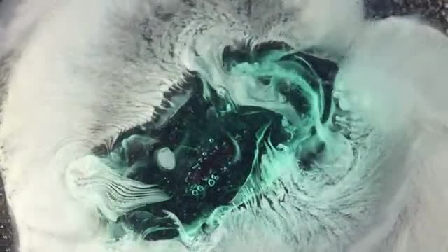 Green and white swirls of a pill dissolving in water.