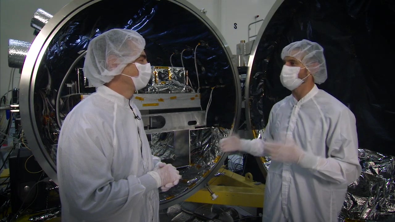 Engineers in cleanroom suits beside starshade hardware in a test chamber
