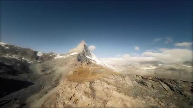 The Matterhorn's pyramid peak above rocky ridges, filmed from a long-range drone.