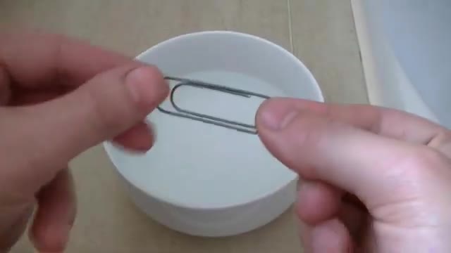 Hands holding a bent wire paperclip over a white bowl.