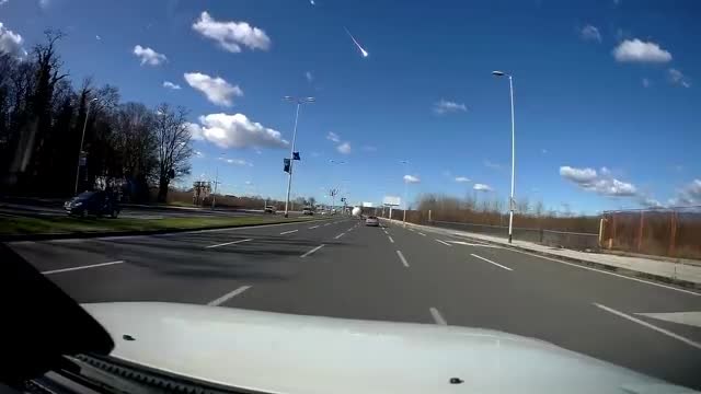 Dashcam view of a highway with a bright meteor streak in the blue sky