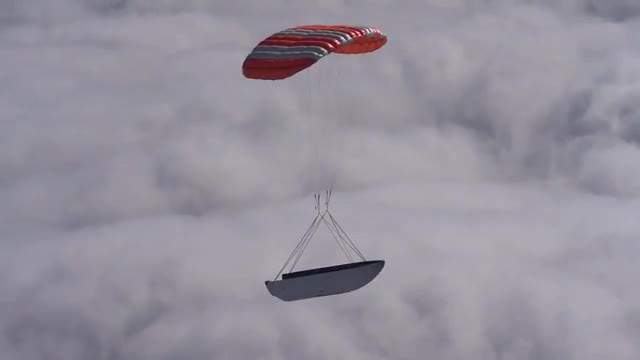 A payload fairing descending under an orange parachute.