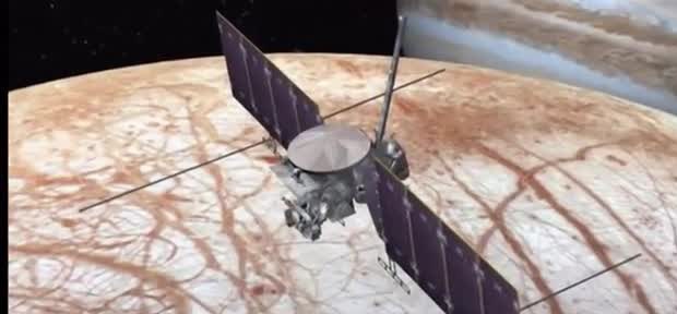 A spacecraft with long solar arrays above Europa's cracked ice, with Jupiter behind.