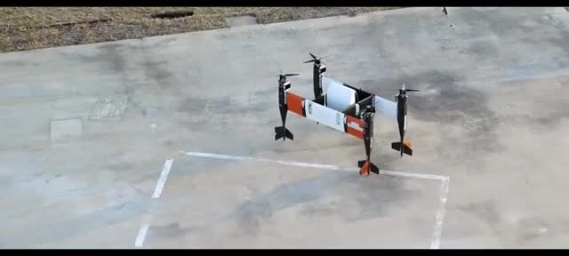A small multi-rotor pod aircraft sitting on a marked concrete pad.