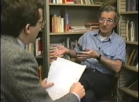 Noam Chomsky speaking during a seated interview in front of bookshelves