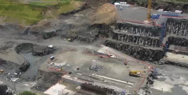An aerial view of a stepped rock excavation with cranes and a concrete lock wall.