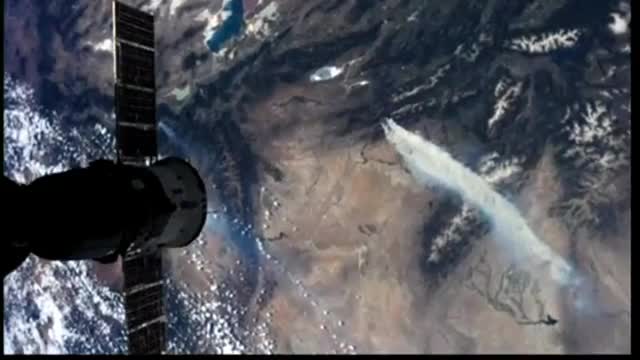 A smoke plume over mountains seen from orbit