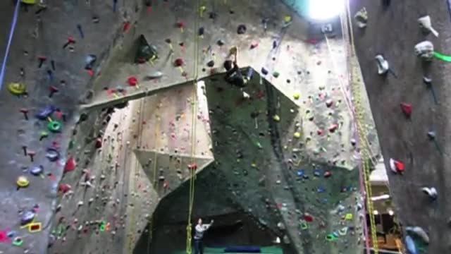 A climber high on an indoor wall with a belayer below